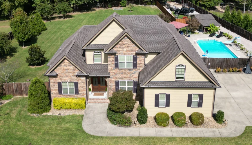 Drone view of a finished roof on a stone and brick home with a backyard pool
