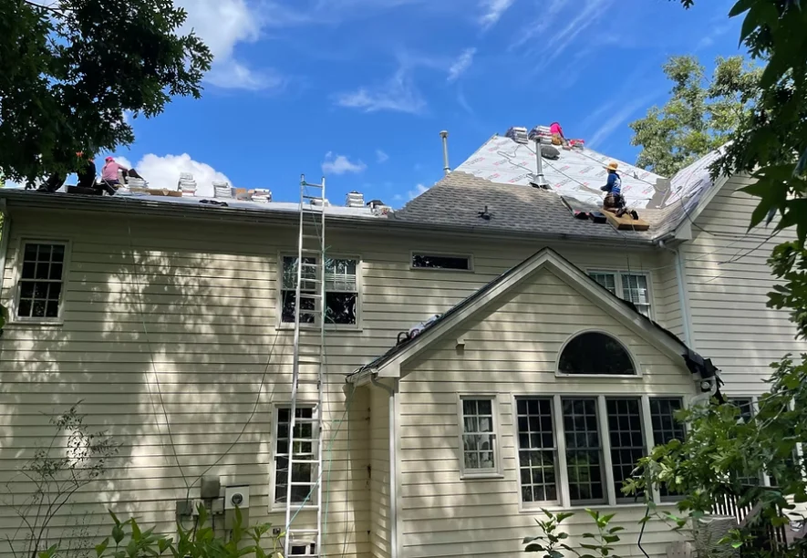 Roofers and ladders on a cream-sided home during a roof replacement